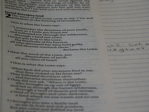 Close-up of hands holding an open Bible with notes and a pen nearby.