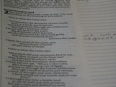 Close-up of hands holding an open Bible with notes and a pen nearby.
