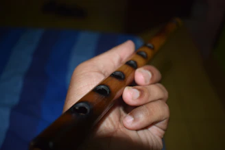 Close-up of hands playing a wooden flute with soft sunlight filtering through leaves.