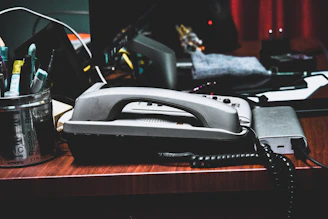 A dimly lit office desk scattered with paper files, a fountain pen, and a classic rotary phone.