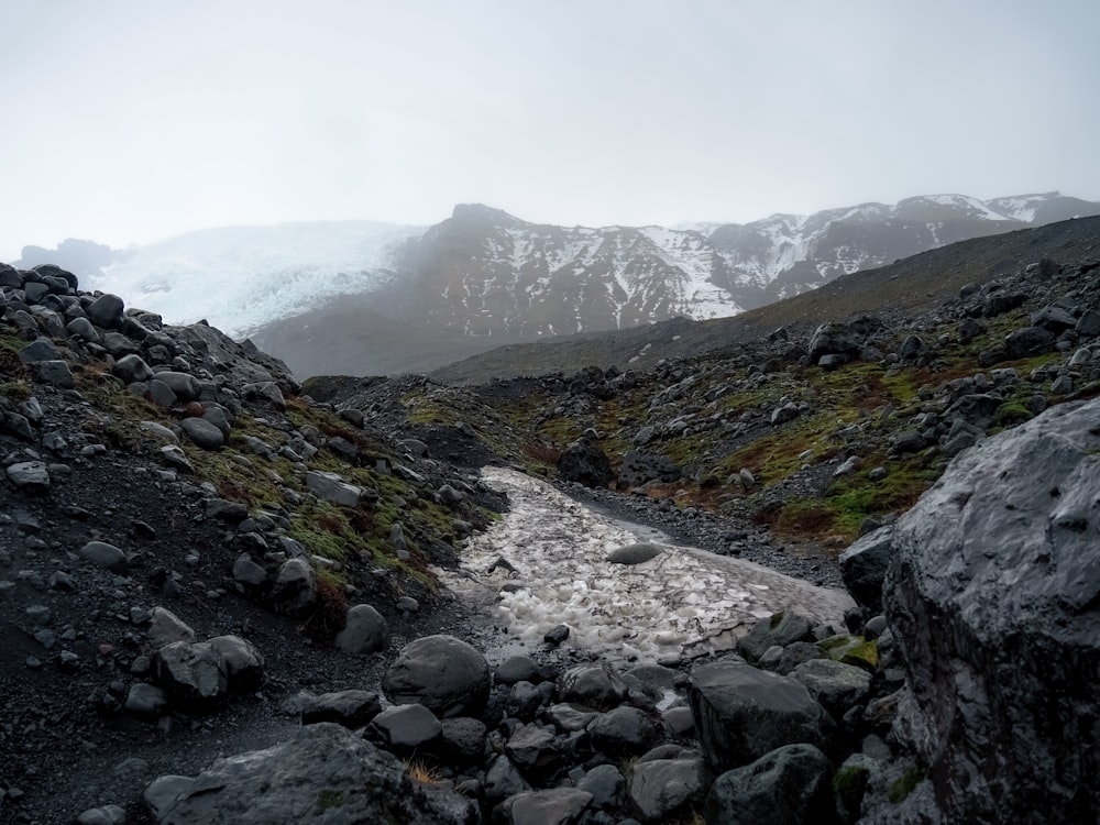 a stream running through a rocky area with mountains in the background