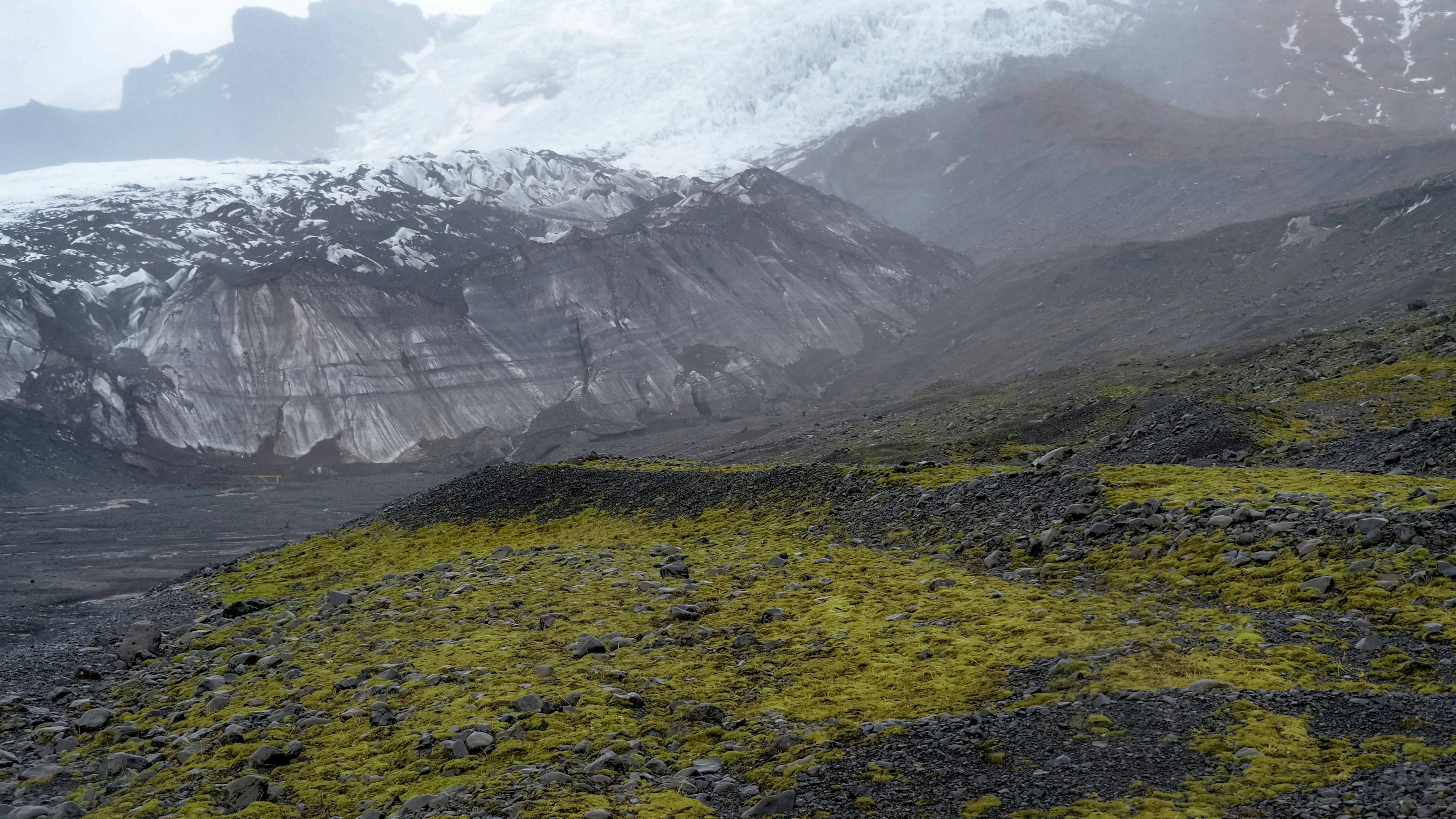 a mountain covered in snow and green moss, Tundra, black sand plain, and the glacier