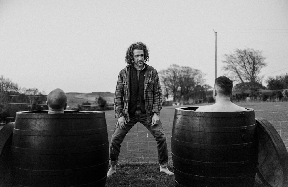 a black and white photo of a man standing between two barrels