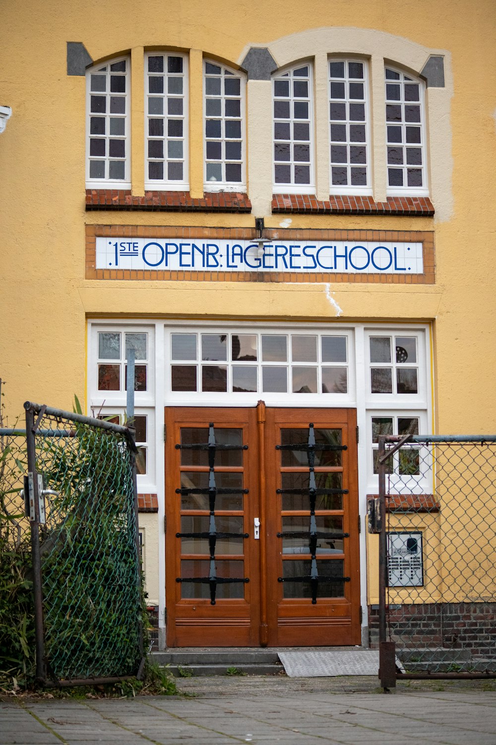 a yellow building with two brown doors and a fence