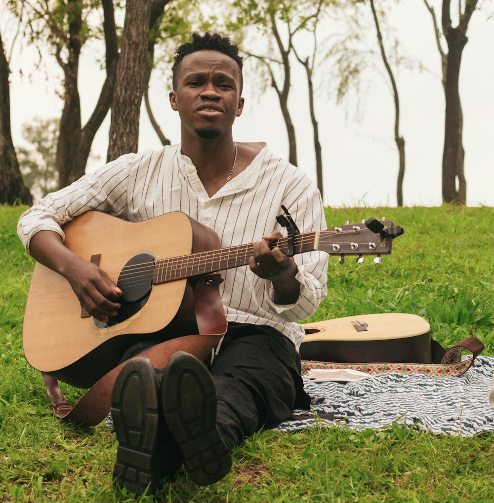 a man sitting in the grass playing a guitar