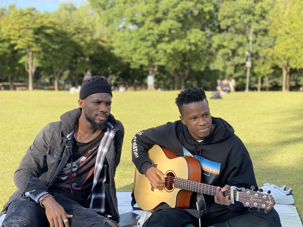 two men sitting on a blanket playing guitars