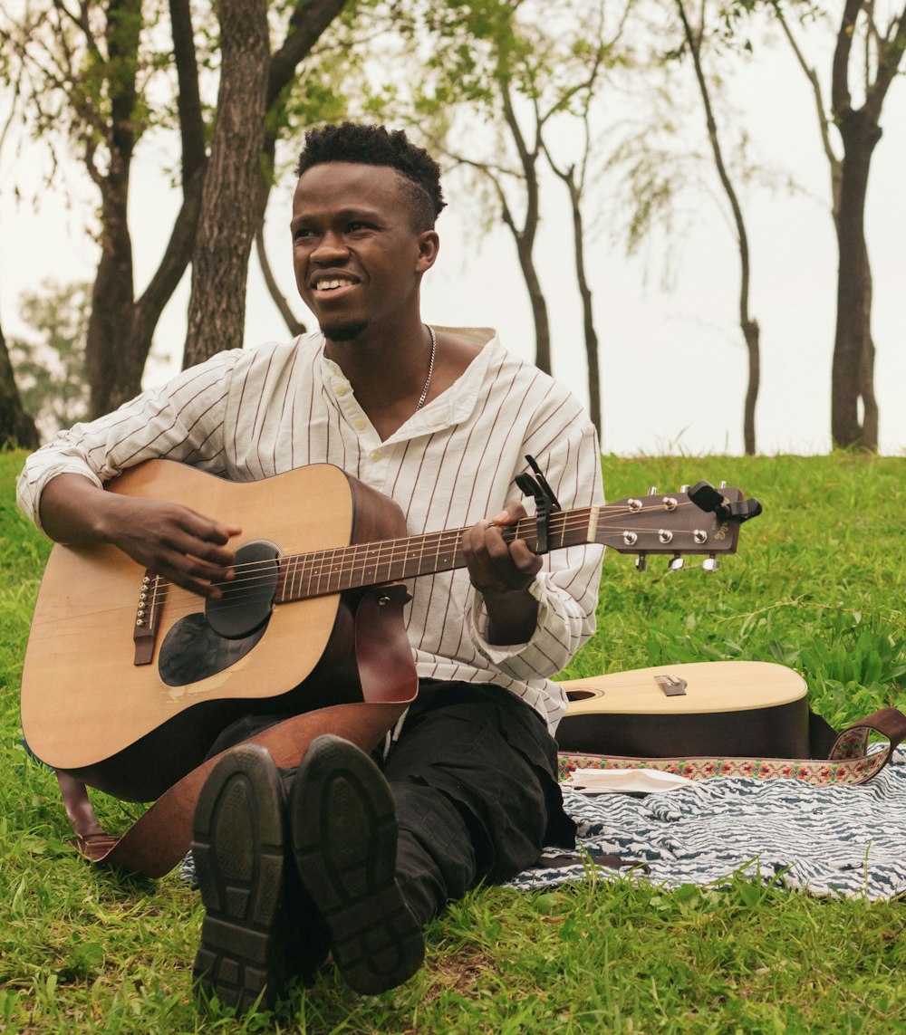 a man sitting in the grass playing a guitar