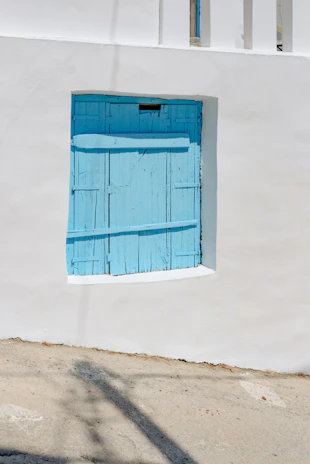 A craftsman painting a wooden shutter outdoors on a sunny day.