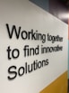 Black 3D text displays the phrase 'Working together to find innovative Solutions' against a geometric background with white, yellow, light blue, and dark blue areas.