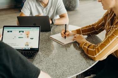 three people sitting at a table with laptops and notebooks