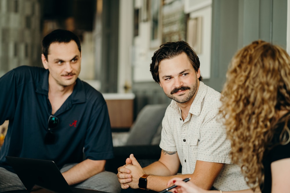 two men and a woman sitting at a table with a laptop