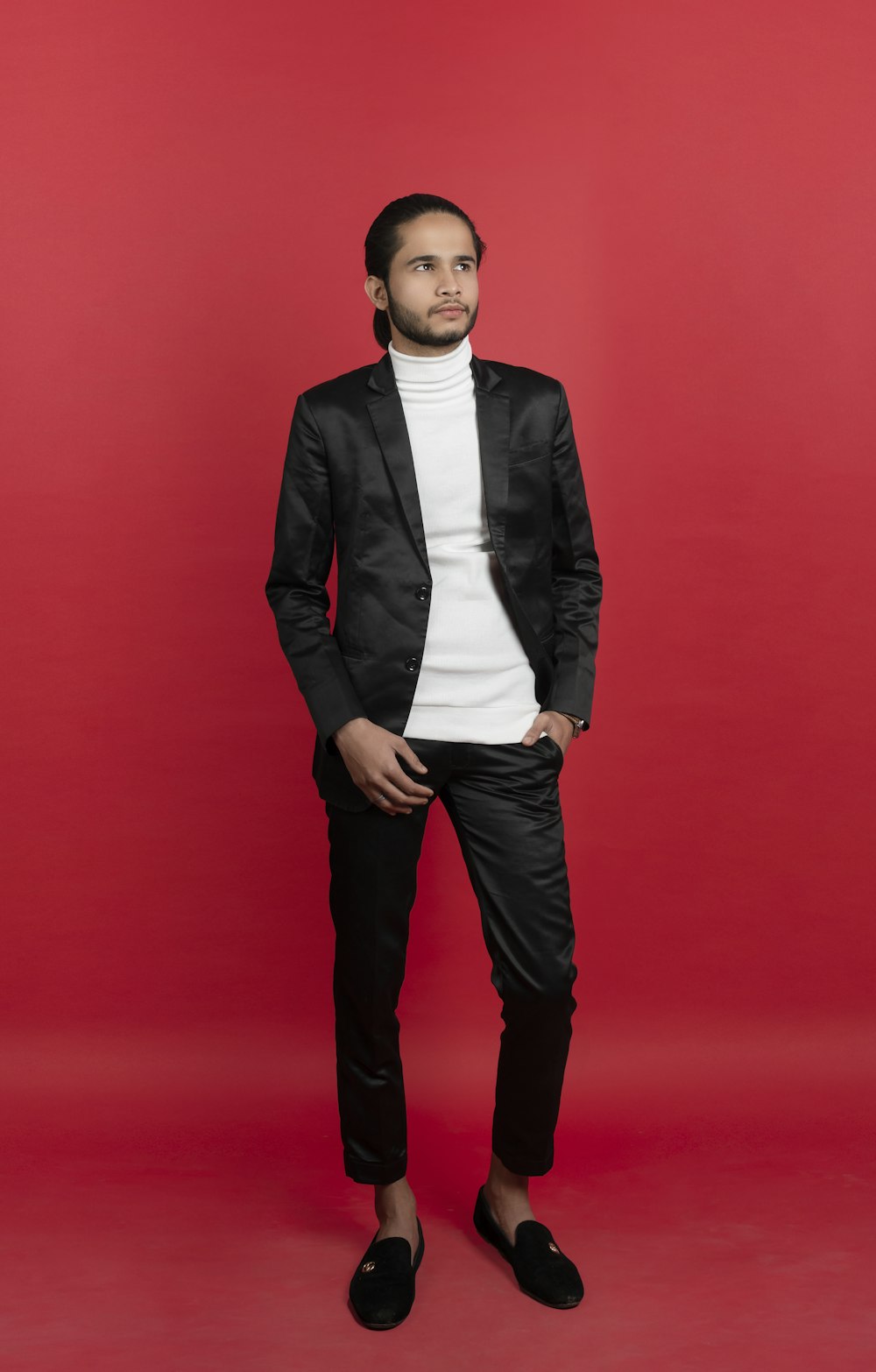 a man in a black suit standing in front of a red background