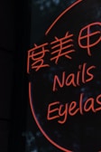 A neon sign displays stylized text in both Chinese characters and English words, with the words 'Nails' and 'Eyelash' visible in bright orange lettering against a dark background.