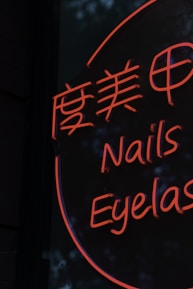 A neon sign displays stylized text in both Chinese characters and English words, with the words 'Nails' and 'Eyelash' visible in bright orange lettering against a dark background.