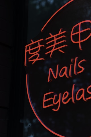 A neon sign displays stylized text in both Chinese characters and English words, with the words 'Nails' and 'Eyelash' visible in bright orange lettering against a dark background.