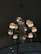 A luxurious chandelier with multiple lights, featuring elegantly decorated lamp shades and crystal ornaments hanging from each arm. The background shows a dark ceiling with high-placed circular fixtures.