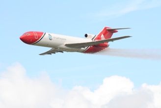 A brightly colored aircraft with red and white markings is flying in a clear blue sky. The plane has the words 'Oil Spill Response' on its side and is releasing a mist or spray from its underside.