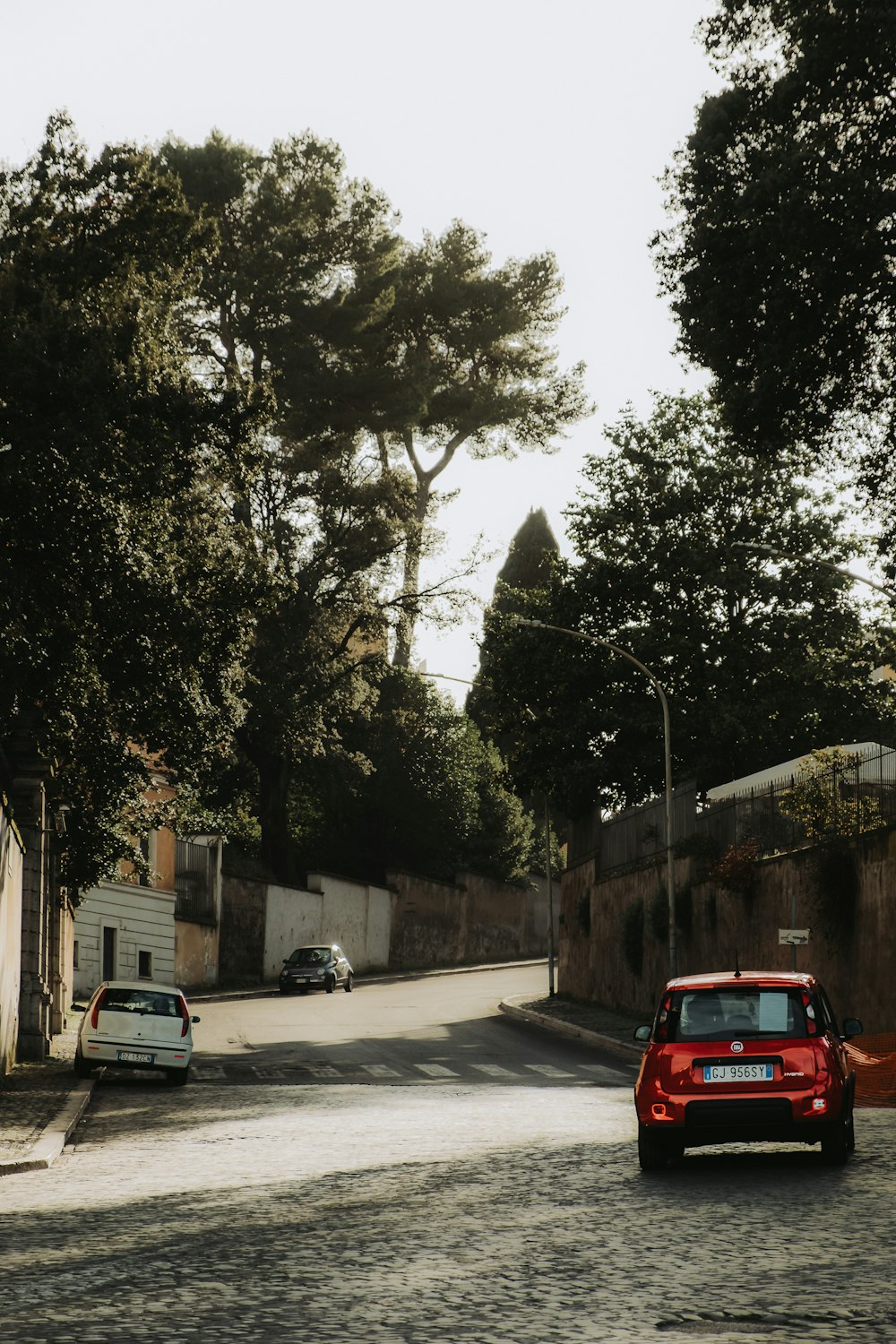 a red car driving down a street next to trees