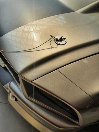 Close-up shot of a carbon fiber car hood with sleek metallic reflections under soft lighting.