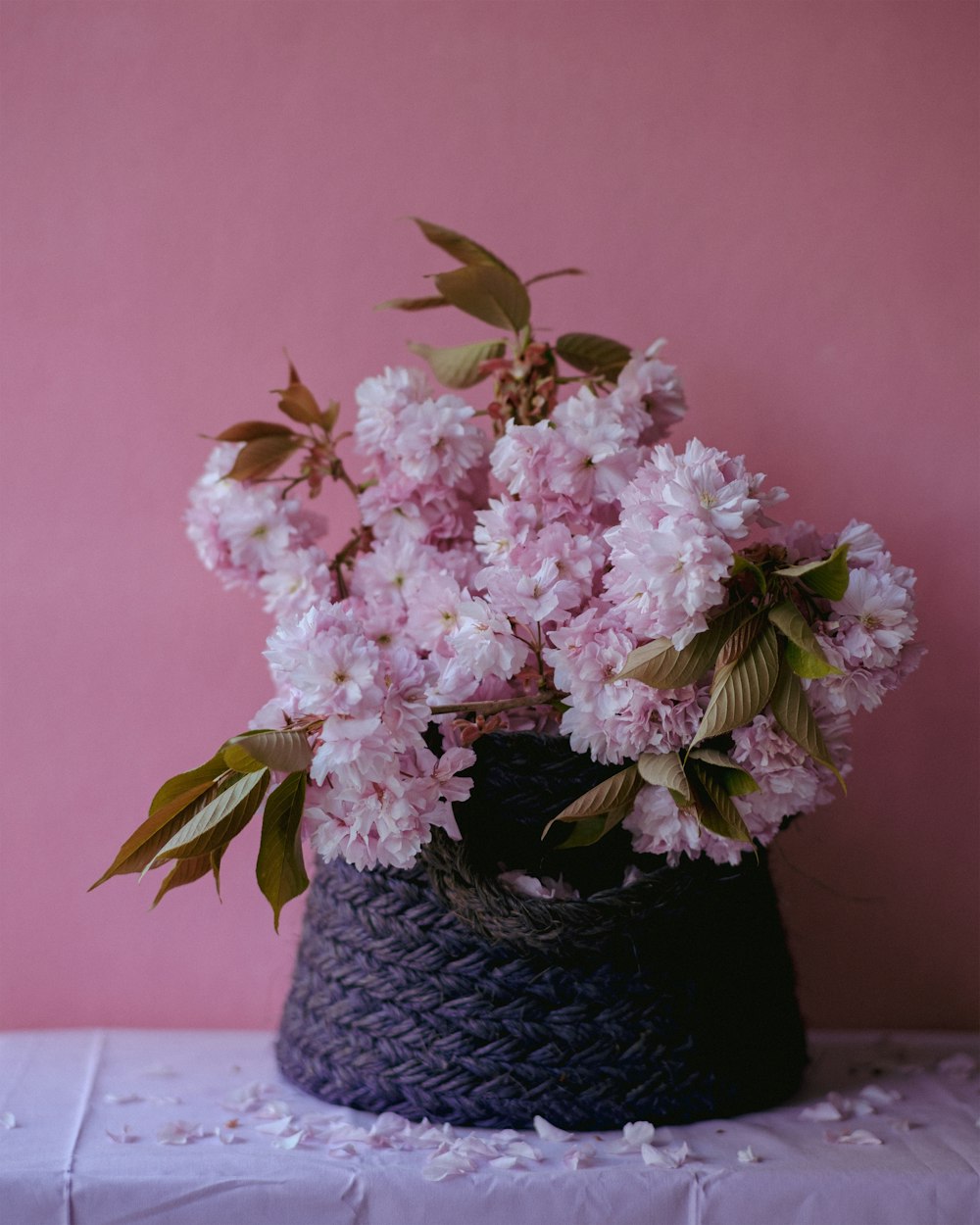 a black basket filled with pink flowers on top of a table