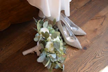 A pair of white bridal shoes adorned with subtle gold accents on a vintage wooden floor.