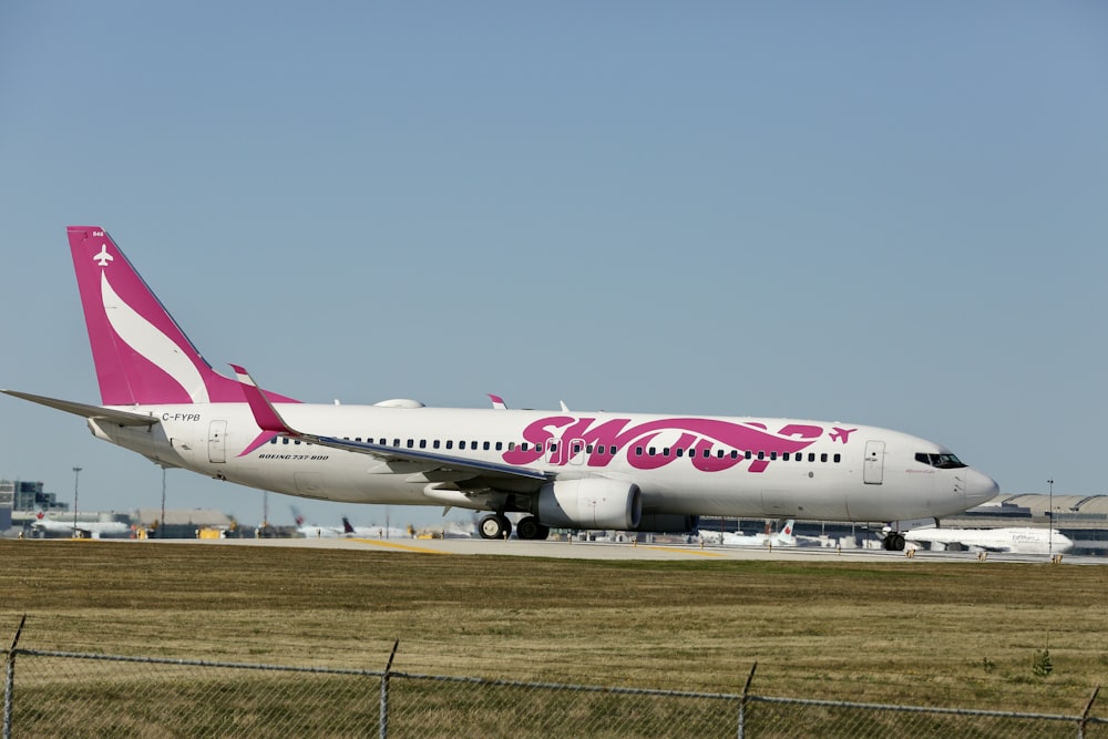 a pink and white plane is on the runway
