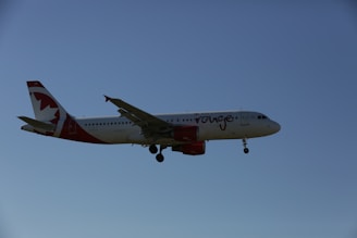 A commercial airplane with white and red livery flying against a clear blue sky. The aircraft is an Airbus model, identified by its twin engines and distinctive tail design.