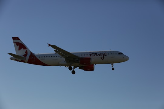 A commercial airplane with white and red livery flying against a clear blue sky. The aircraft is an Airbus model, identified by its twin engines and distinctive tail design.