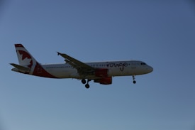A commercial airplane with white and red livery flying against a clear blue sky. The aircraft is an Airbus model, identified by its twin engines and distinctive tail design.