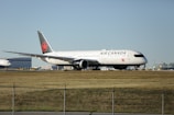 An Air Canada aircraft positioned on a runway at an airport, with buildings and infrastructure visible in the background under a clear sky.