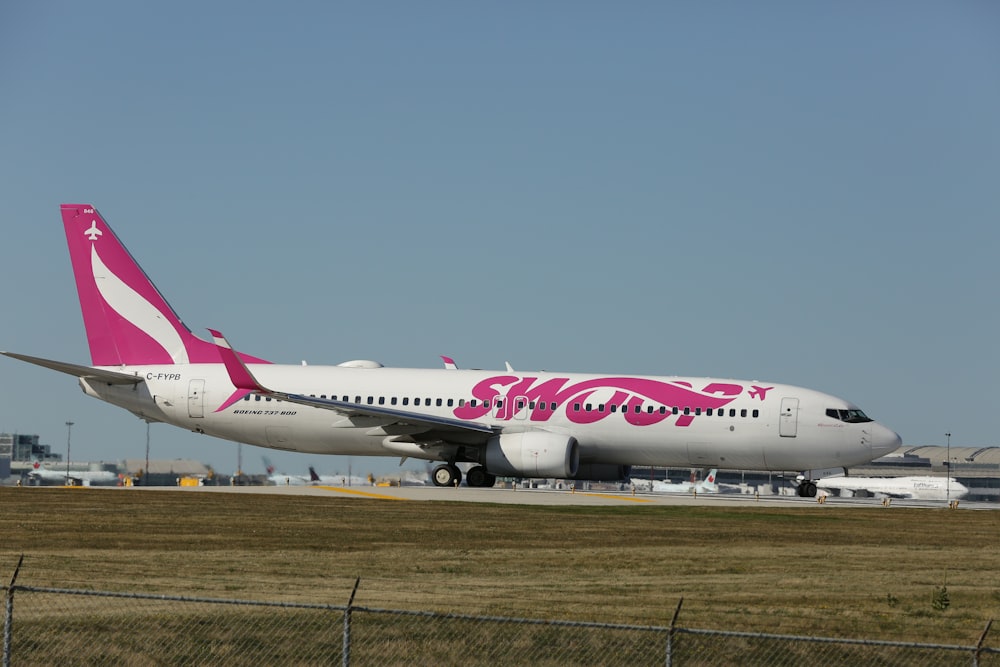 a pink and white airplane is on the runway
