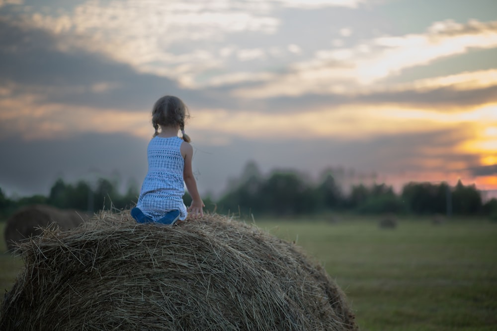 a little girl sitting on a bale of hay