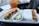 A metal tray holds a partially wrapped sandwich with shredded meat and greens, a small cup of sliced cucumbers, alongside a drink in a plastic cup with a brand logo.