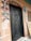 A black, ornately carved door set in a brick wall, decorated with colorful triangular flags spelling 'WELCOME' on the left side. Above the door, the letters 'ACCESS' are arranged in a decorative pattern. To the right, there is a decorative hanging and a partially visible colorful abstract art piece.