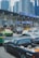 A busy toll booth area with multiple lanes, cars lined up, and overhead blue signs labeled 'Easy Pass' in Thai and English. Skyscrapers are visible in the background, indicating an urban setting. Vehicles of various types, including a black pickup truck, a green and yellow taxi, and several sedans, are present.