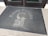 A doormat placed in front of a glass door features the text 'Rusty Pelican Cafe' with an illustration of a pelican perched on a post.