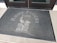 A doormat placed in front of a glass door features the text 'Rusty Pelican Cafe' with an illustration of a pelican perched on a post.