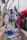 Several individuals are engaged in a community cleanup, collecting trash from a gutter. They are dressed casually and are focused on picking up plastic bottles and litter. The setting is outdoors, with bags to collect the trash.