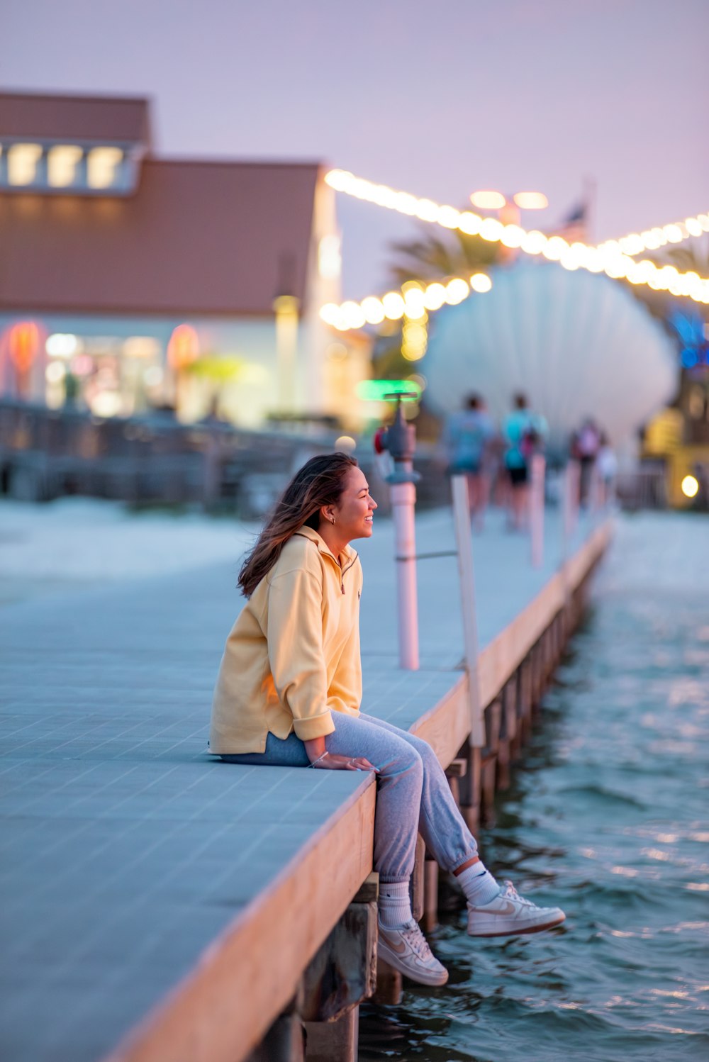 a woman sitting on a pier next to a body of water