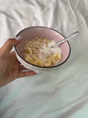 Close-up of hands holding a bowl of millet porridge topped with fresh fruit.