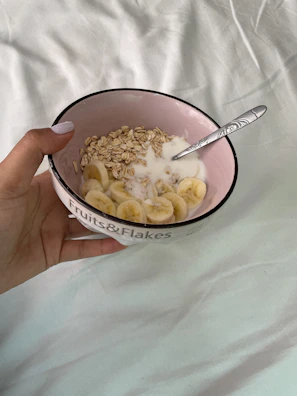 Close-up of hands holding a bowl of millet porridge topped with fresh fruit.