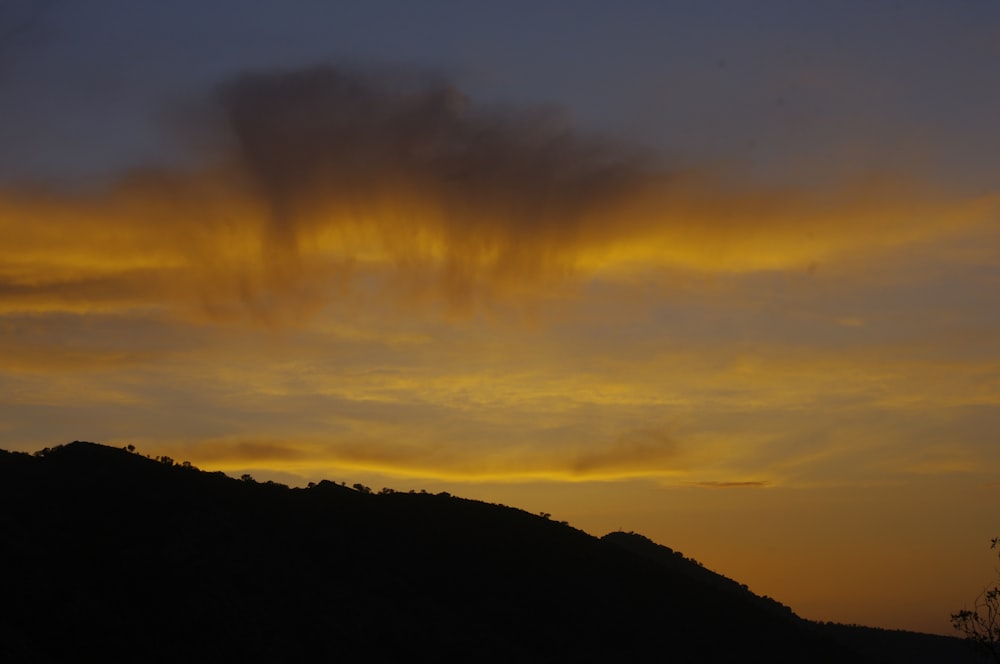 the sun is setting over a hill with a tree in the foreground