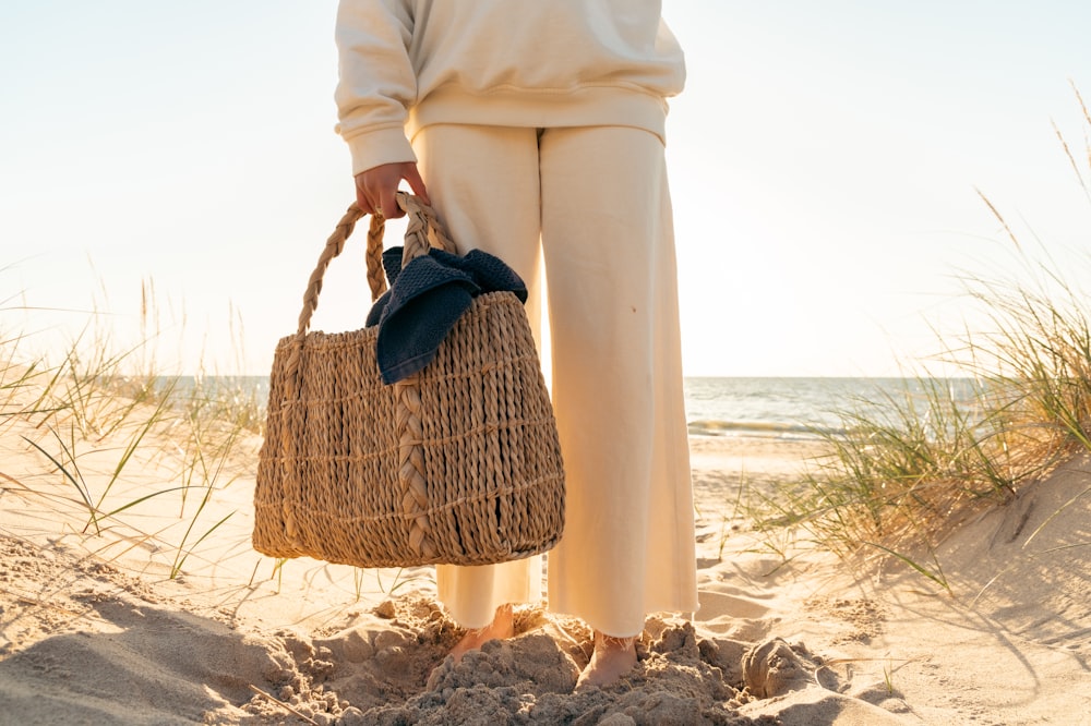 a person standing on a beach holding a wicker bag