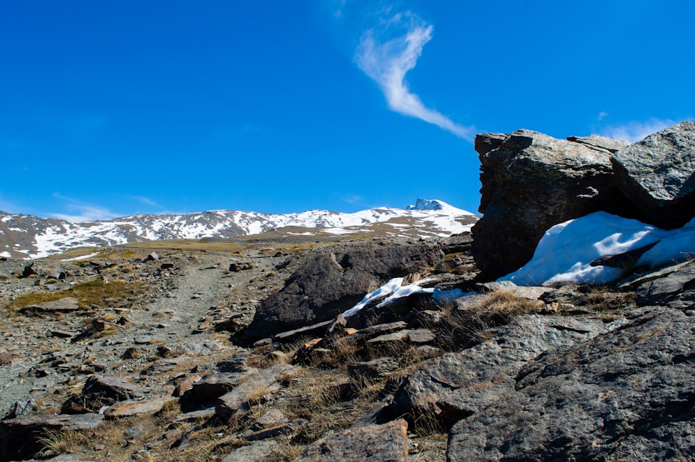 a rocky area with snow on the ground and mountains in the background