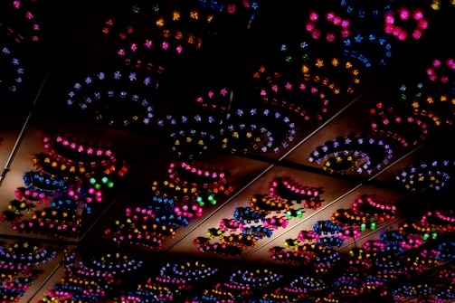 A ceiling adorned with a series of colorful, decorative lights forming intricate patterns. The lights emit in vivid hues, arranged in swirling, circular shapes that add a whimsical and festive atmosphere.