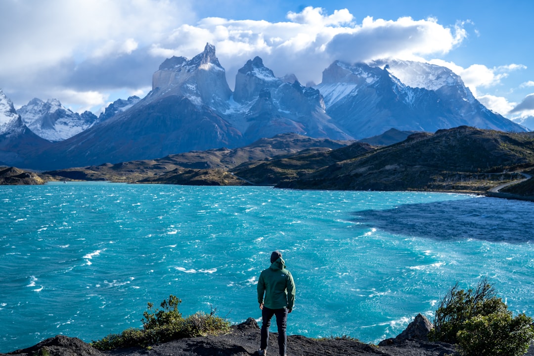 a man standing on top of a mountain next to a lake,