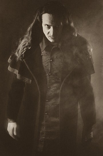 A moody, shadowy scene featuring a model draped in dark, intricate gothic attire from the Coven Collection.