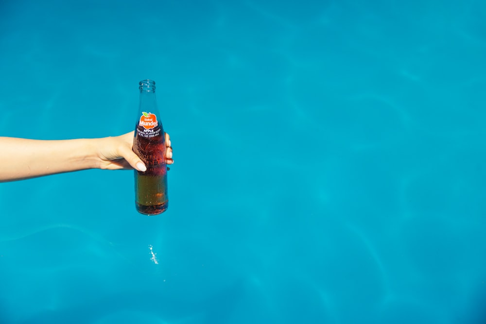 une personne tenant une bouteille de bière dans l’eau