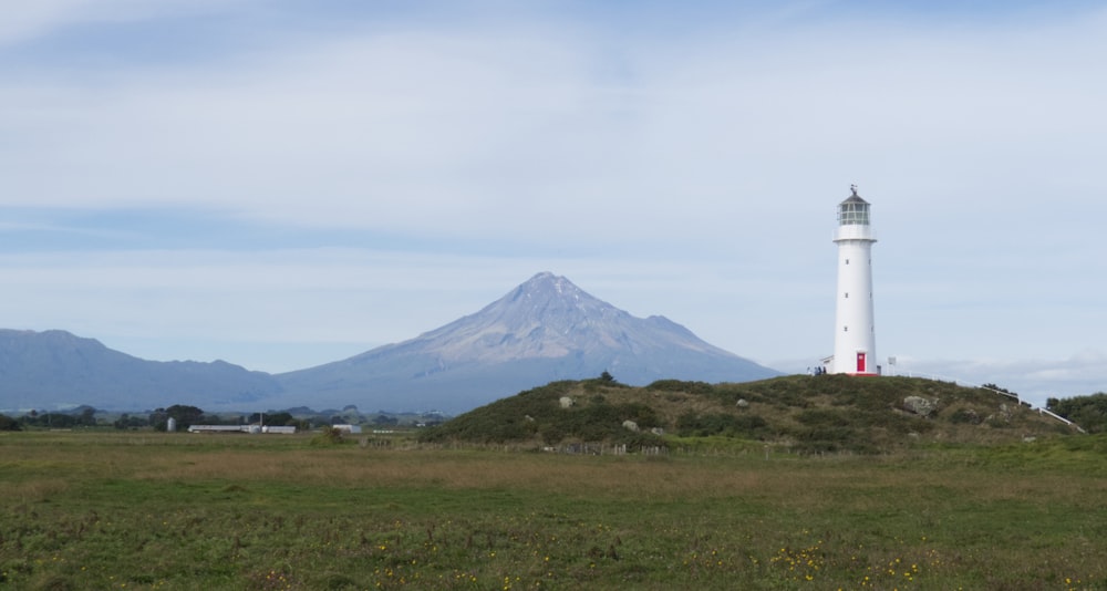 a lighthouse on a grassy hill with a mountain in the background