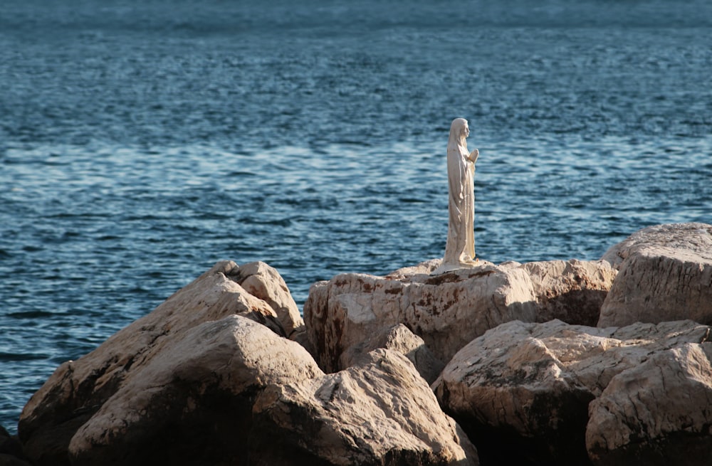 a statue of a woman standing on a rock by the ocean